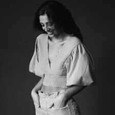 smiling trendy woman standing with hands in pockets in studio