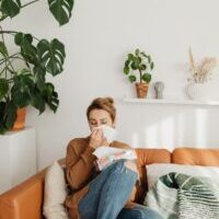 woman sitting on sofa and blowing her nose into a tissue